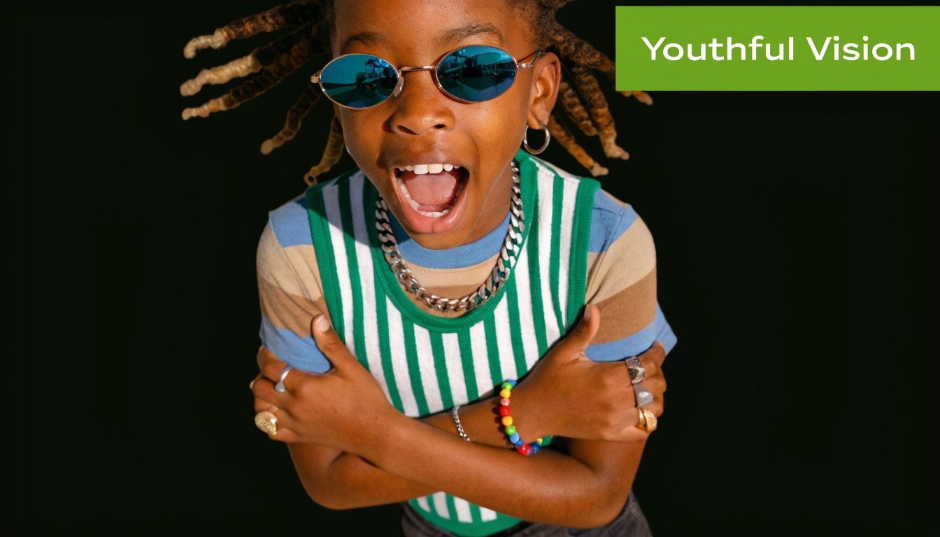 A young person with dreadlocks wearing stylish small sunglasses and a colorful striped shirt posing confidently.